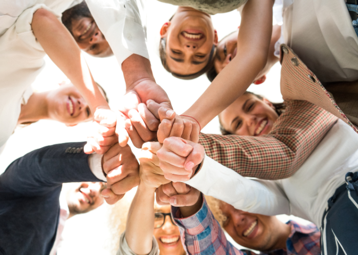 Group of people smiling and putting their hands together at a central point